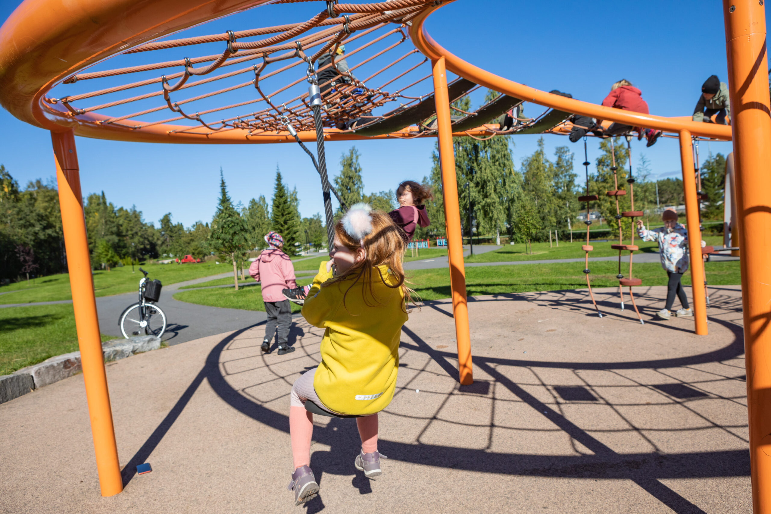 Barn med ryggen mot kameran som leker i en klätterställning. Blå himmel och sol.